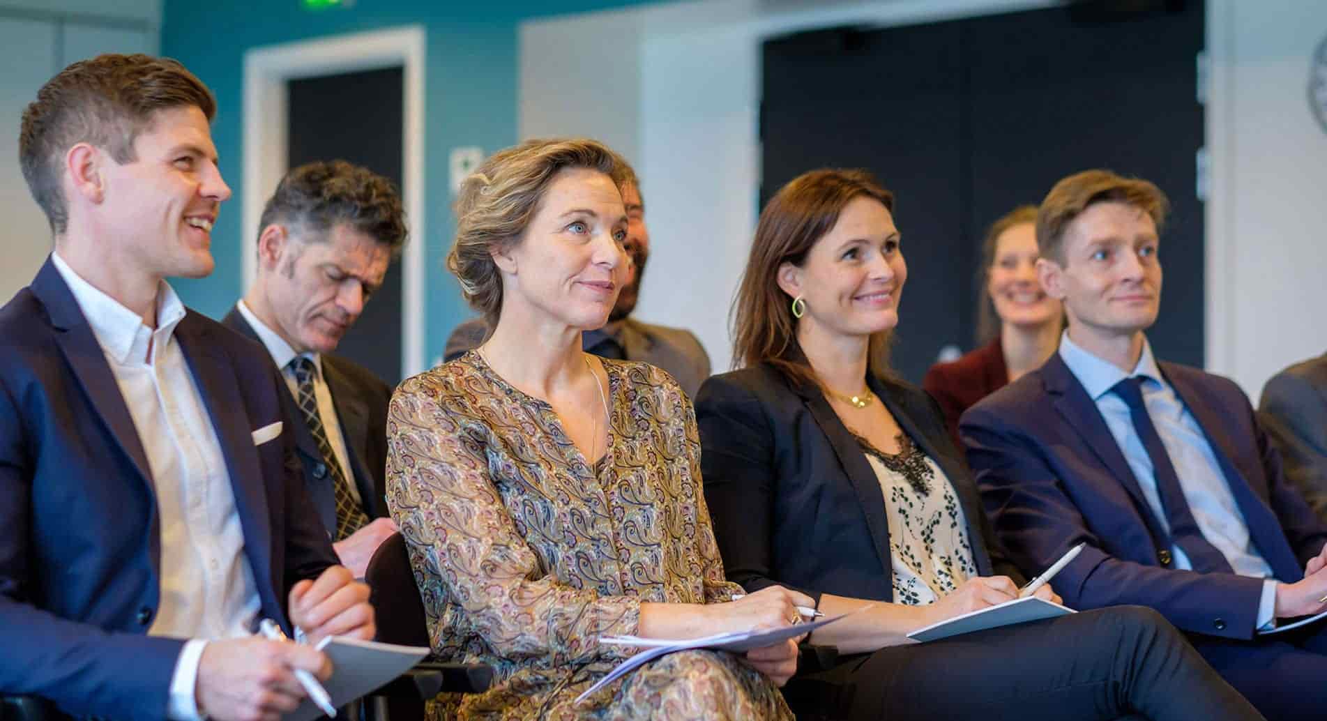 Professionelle deltagere lytter opmærksomt under konference på Sjælland i moderne mødelokale.