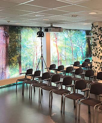 Mødelokale i Roskilde Kongres- og Idrætscenter på Sjælland med stoleopsætning, projektorer og grønne detaljer, klar til konference eller seminar.