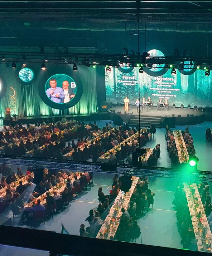 Hal D med scene, storskærme og lange bordrækker til stort firmaevent