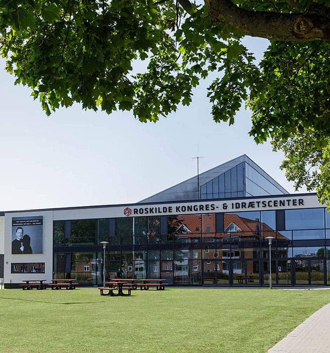 Facade af Roskilde Kongres- og Idrætscenter på Sjælland med grønne udearealer og plads til konferencer, kurser og erhvervsarrangementer.